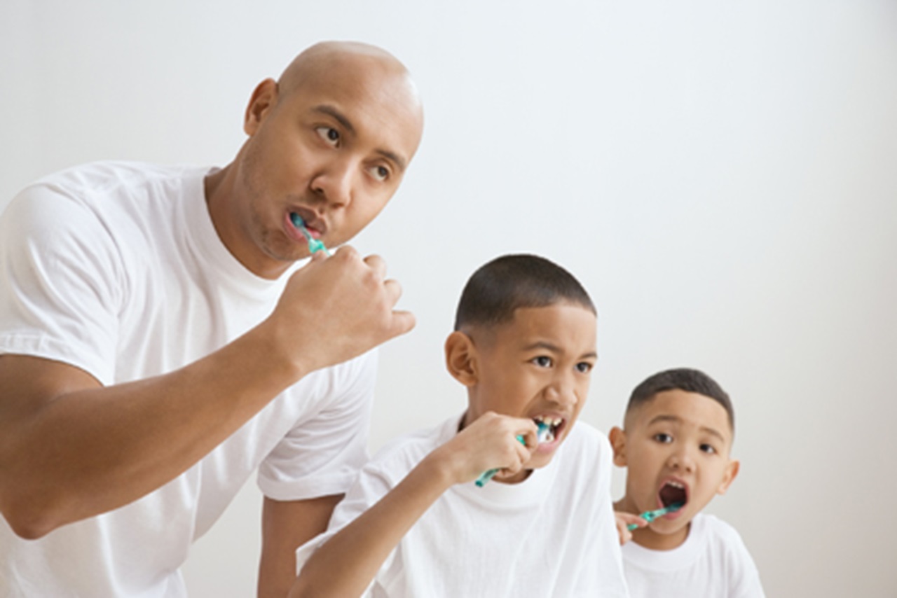 father and sons brush their teeth together