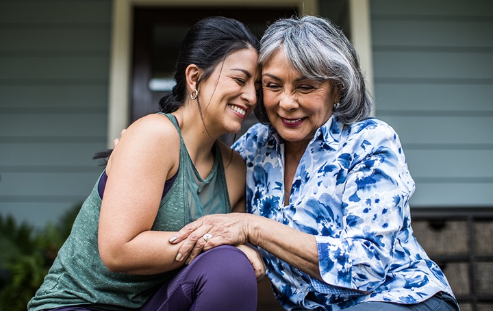 Older mother and daughter sitting on front stoop embracing