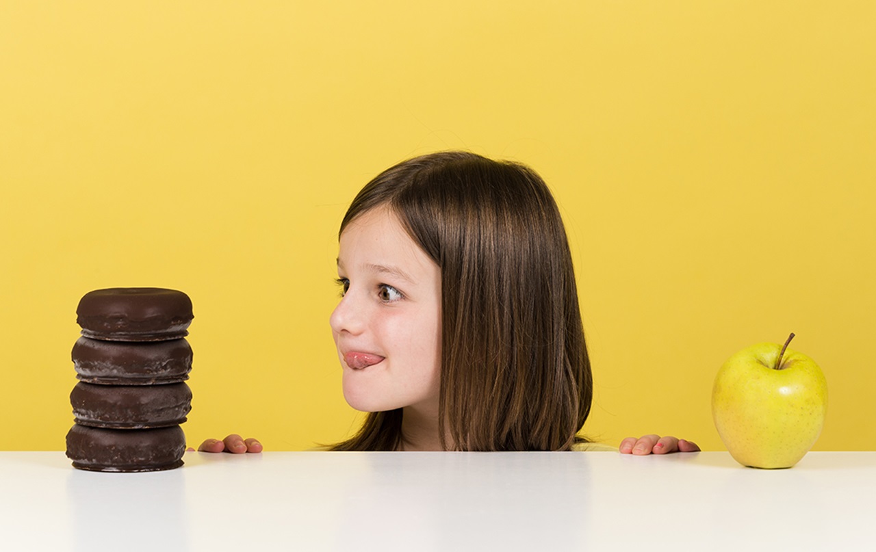 Girl eyeing giant stack of chocolate cookies instead of apple