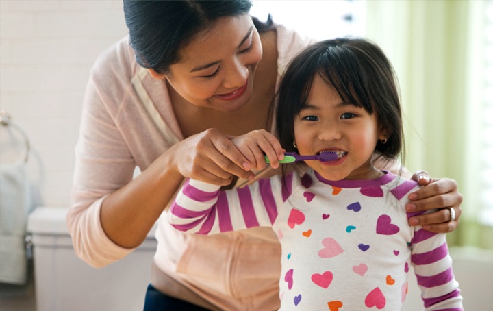 A young child getting help while brushing her teeth
