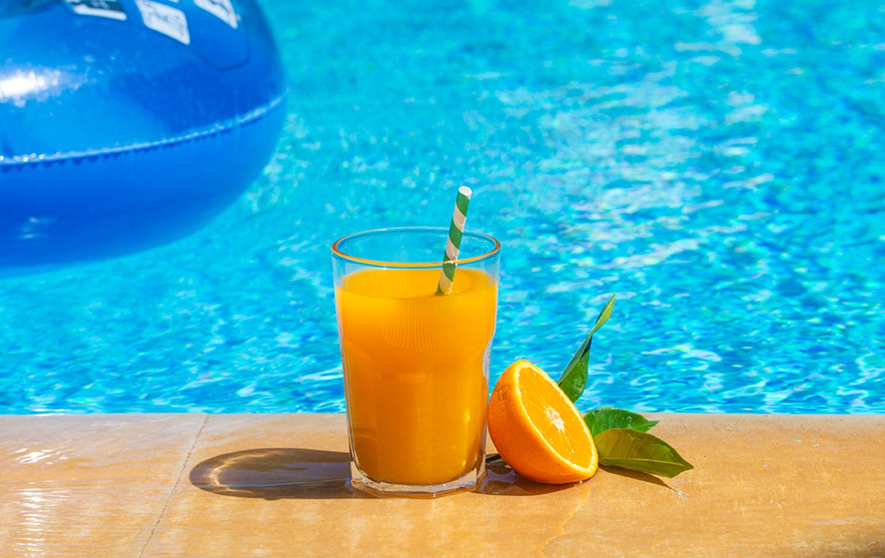Glass of orange juice next to pool