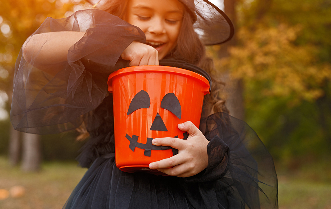 Girl in witch costume looking in a Halloween bucket