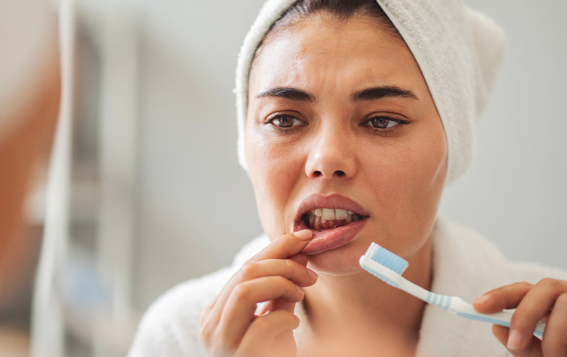 Woman examining gums while brushing teeth.