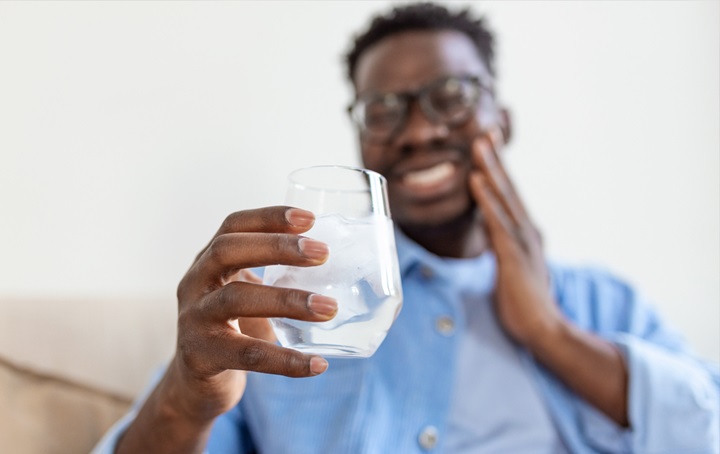 A guy seems to have a sensitive tooth after taking a drink of a cold beverage