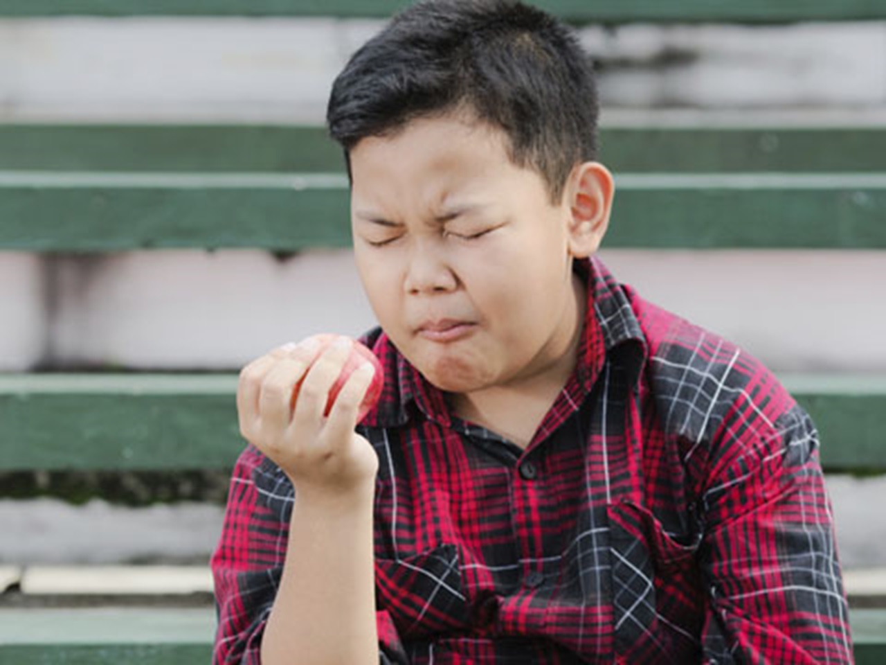 Boy winces while eating an apple